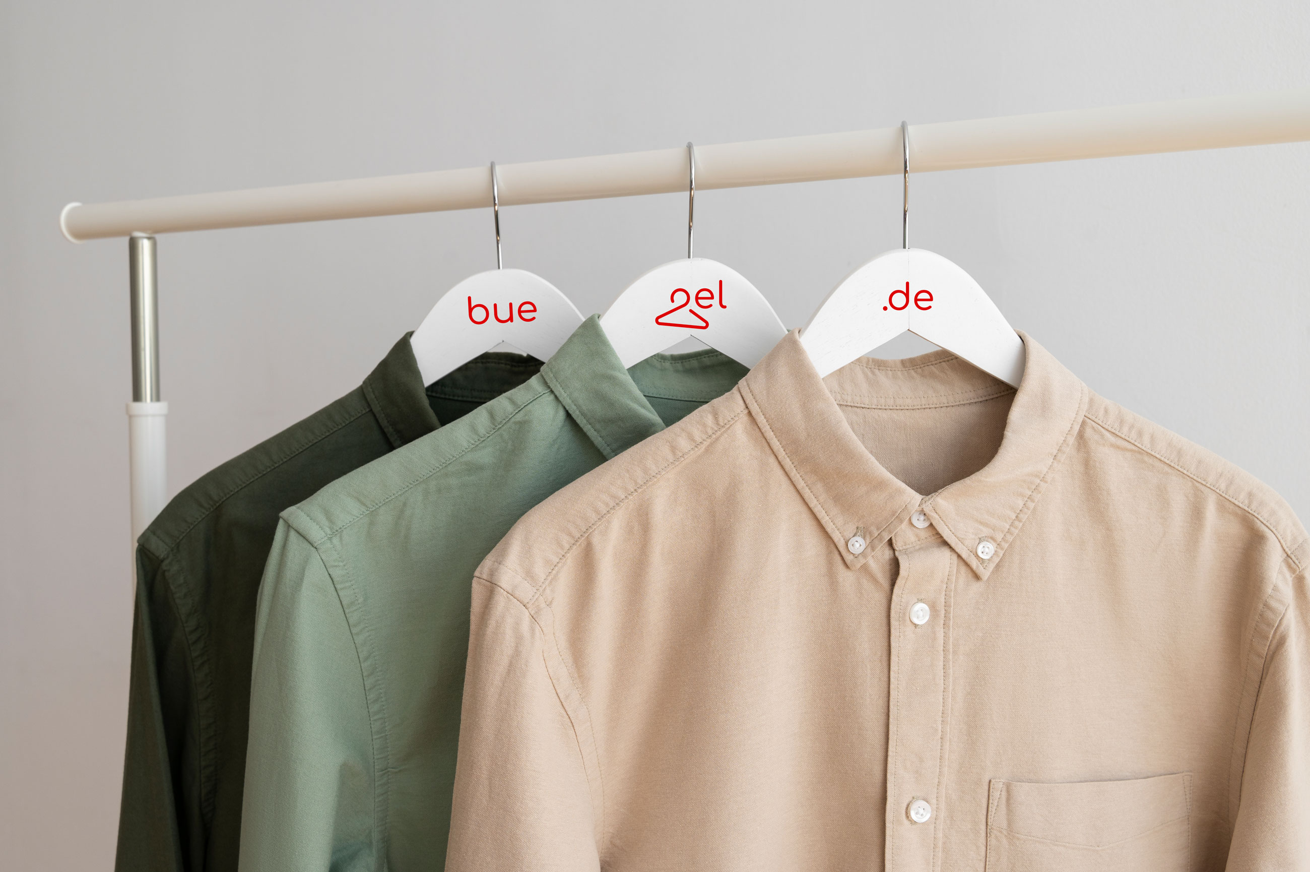 Druckkleiderbügel Drei Hemden an einer Kleiderstange mit weißen Kleiderbügeln. Diese sind mit "buegel.de" beschriftet